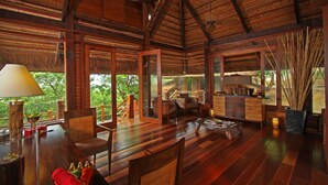 Amplia habitación con pisos de madera, un comedor y ventanas grandes que ofrecen vistas a zonas verdes.