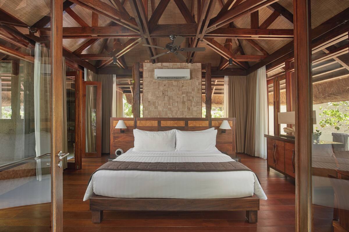 A wooden-framed bedroom with a large bed, a ceiling fan, and an air conditioning unit.
