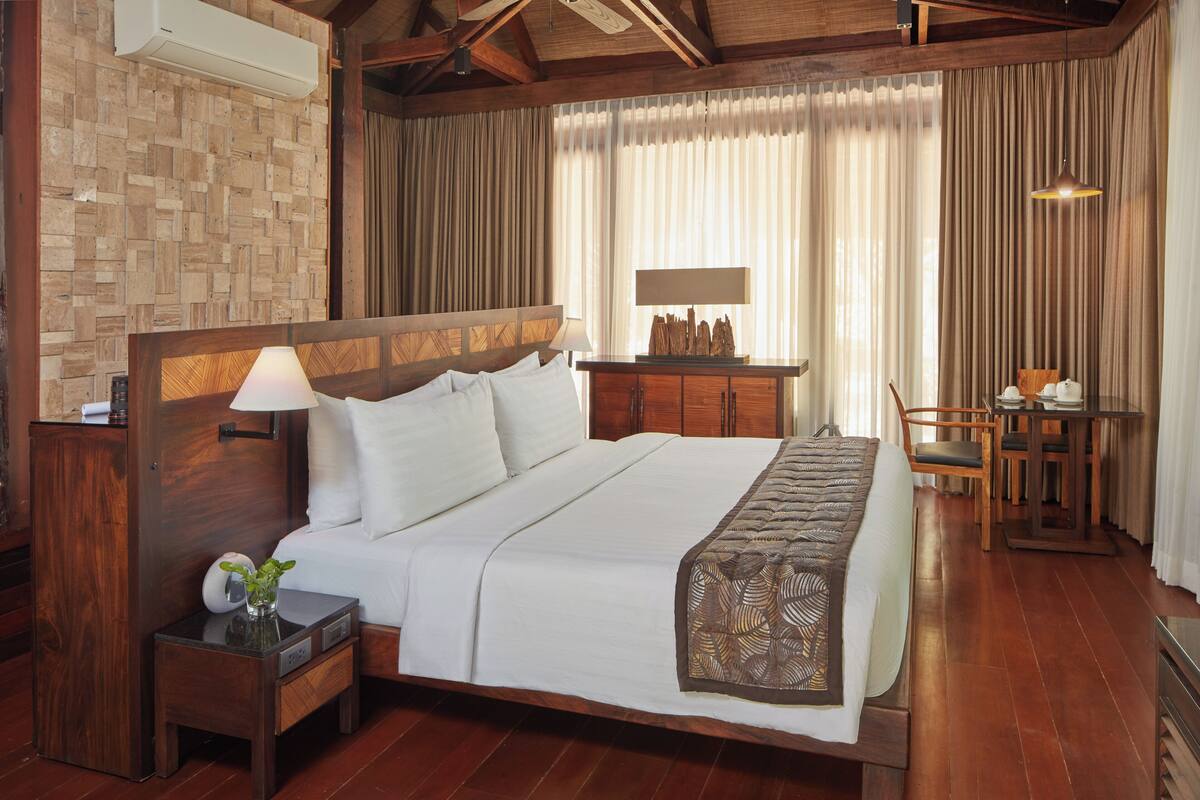 A spacious bedroom with a large bed, wooden headboard, bedside tables, and a desk with chairs.