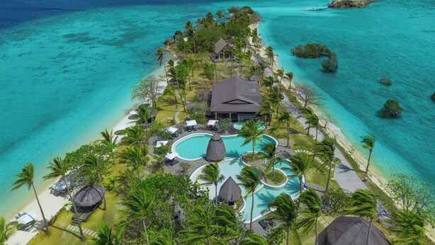 Un resort tropical con piscina, palmeras y una playa.