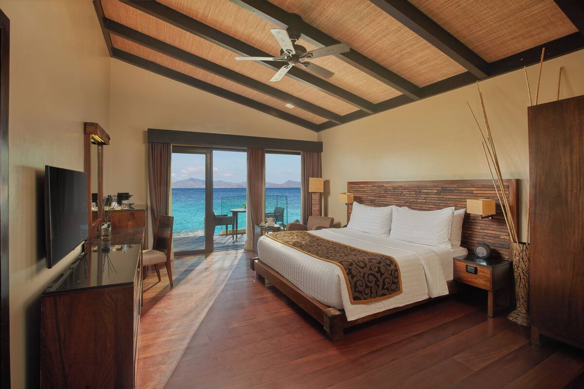 A spacious bedroom with a large bed, a TV, and a view of the sea.