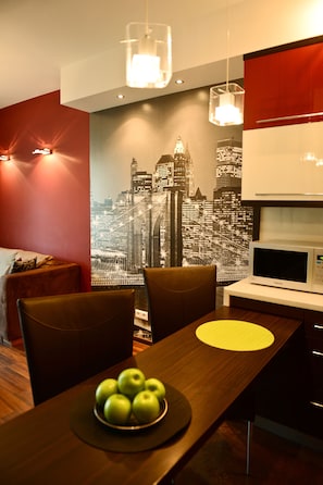A modern kitchen with a microwave, a dining table with a bowl of apples, and a cityscape mural on the wall.
