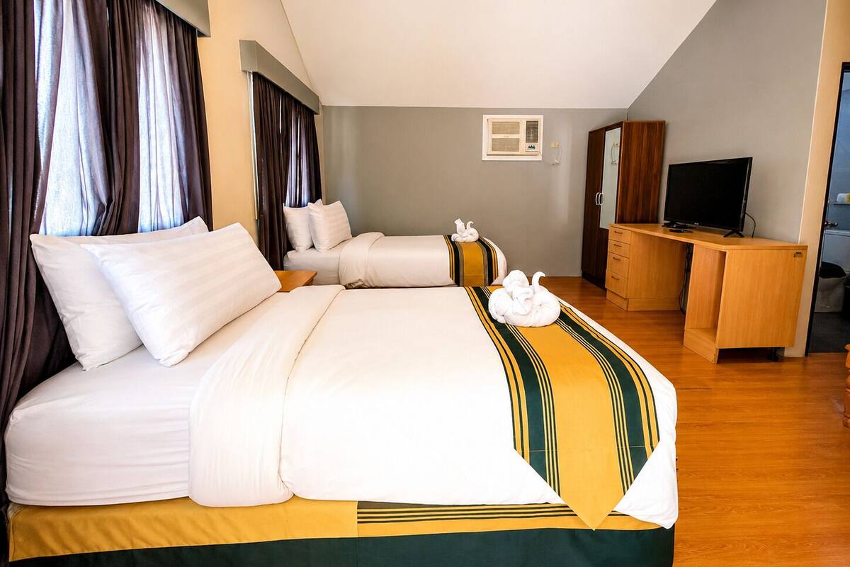 A hotel room with a large bed, a desk, a television, and a window with curtains.