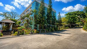 A modern building with glass windows, surrounded by tropical plants and a clear blue sky. - Forest Crest Nature Hotel and Resort (Nasugbu)