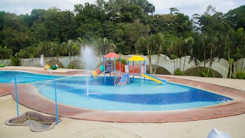Explore a vibrant water park with a central pool area surrounded by play structures and lush tropical vegetation.