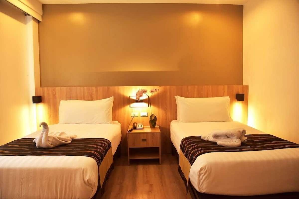 Ein Hotelzimmer mit zwei Einzelbetten, einem Nachttisch mit Lampe und einem hölzernen Kopfteil.