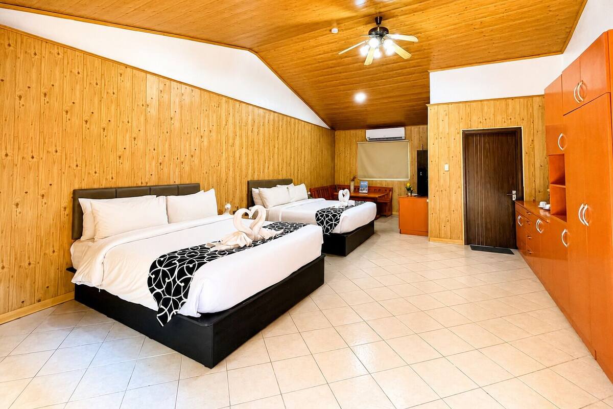 A hotel room with two beds, wooden walls, a ceiling fan, and a wardrobe.