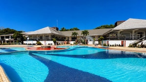 A large swimming pool with a tiled deck, surrounded by buildings with a flat roof and a clear blue sky. - Forest Crest Nature Hotel and Resort (Nasugbu)