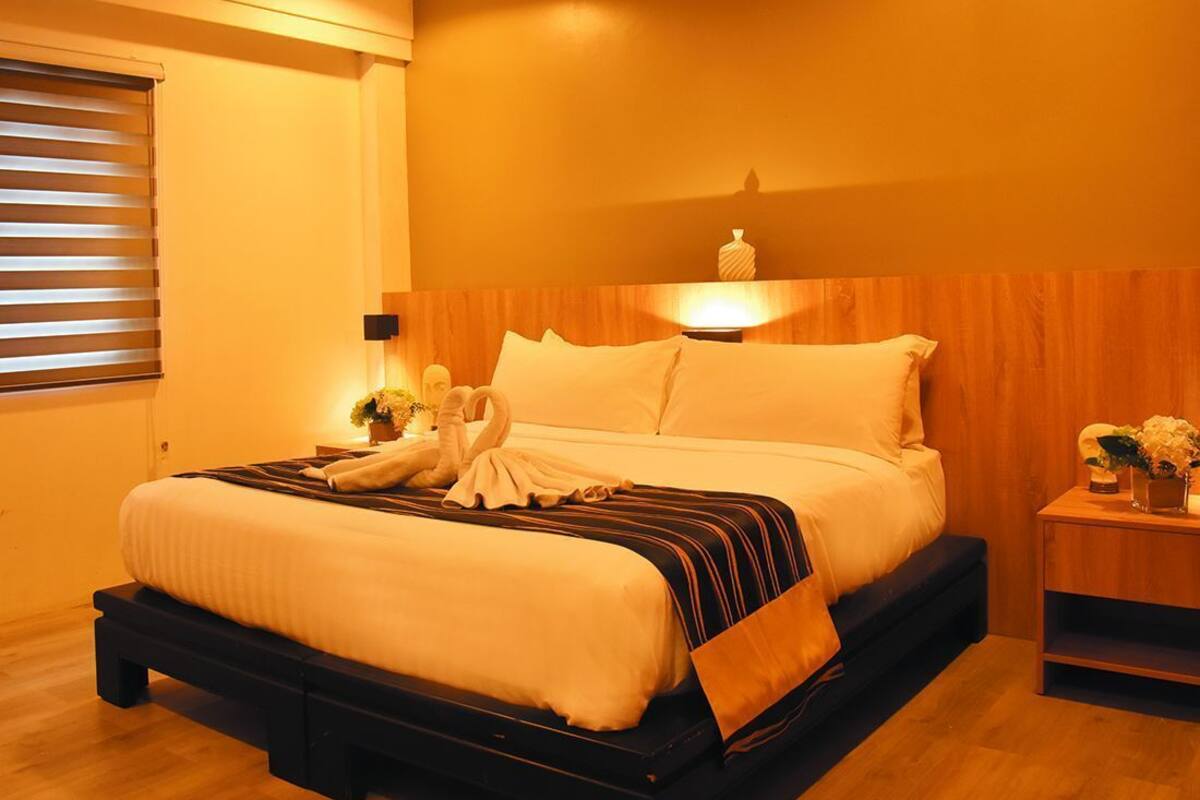 A hotel room with a bed, bedside table, and a wall-mounted light fixture.