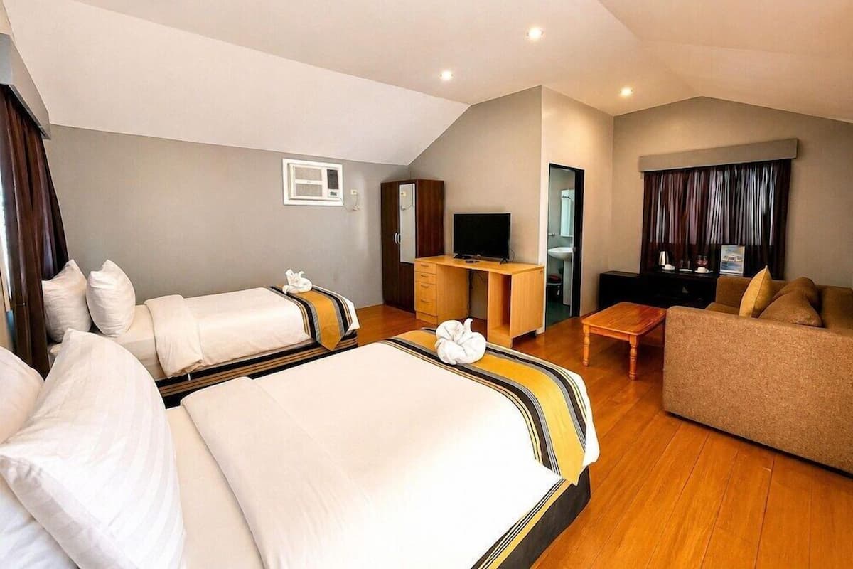 Ein Hotelzimmer mit zwei Betten, einem Sofa, einem Schreibtisch und einem Fernseher.