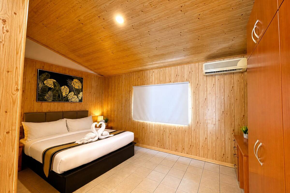A wooden-paneled room with a bed, a wall-mounted air conditioner, and a window with a white blind.