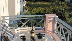A round table with a bottle, teapot, and cups on a balcony with white railings and a view of the sea. - Cybele Suites & Apartments (Ierapetra)