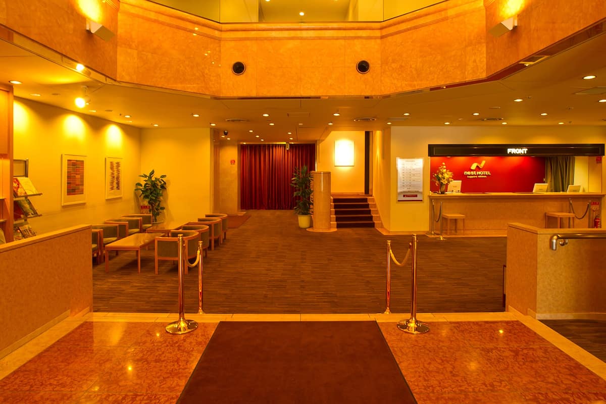 Eine Hotelhalle mit einer zentralen Treppe, einer Rezeption und einer Sitzecke.