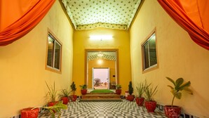 Un pasillo con baldosas de diseño, plantas en macetas y una puerta central con alfombra verde.