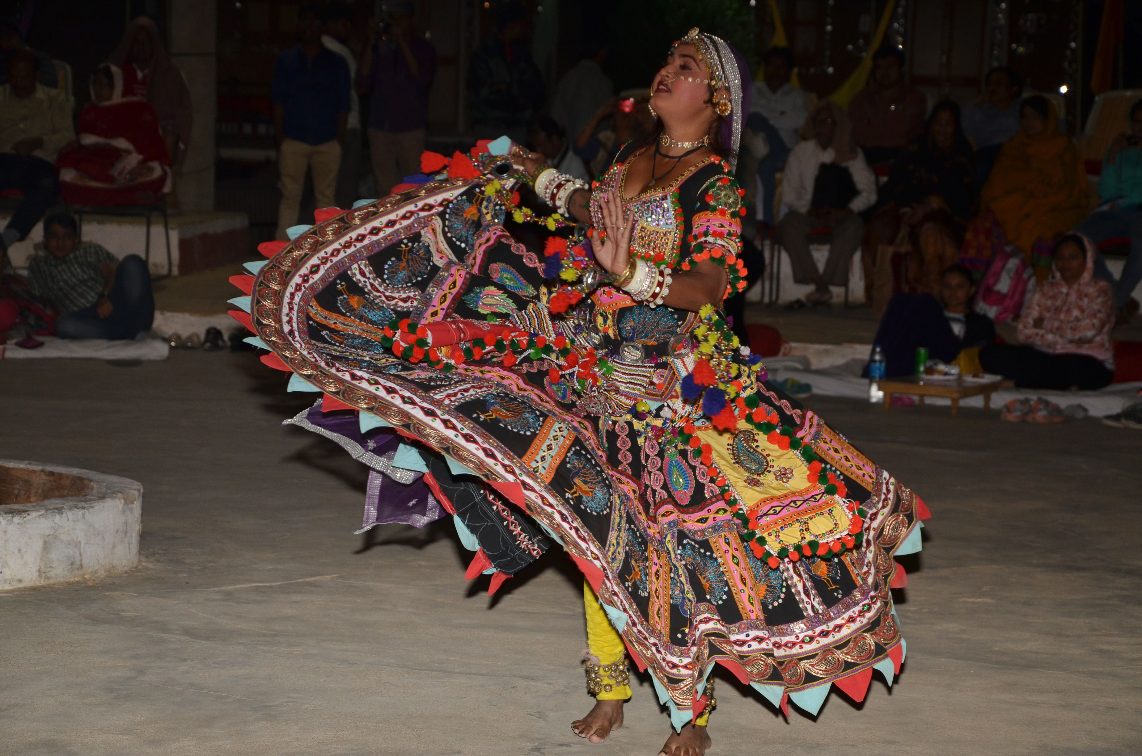 Una persona vestida con un traje tradicional y colorido actuando al aire libre frente a un público.