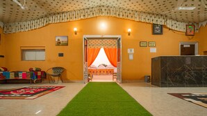 A hotel lobby with a green carpet leading to a reception desk, a check-in counter, and a room entrance with orange curtains. - K K Resorts & Camp (Jaisalmer)