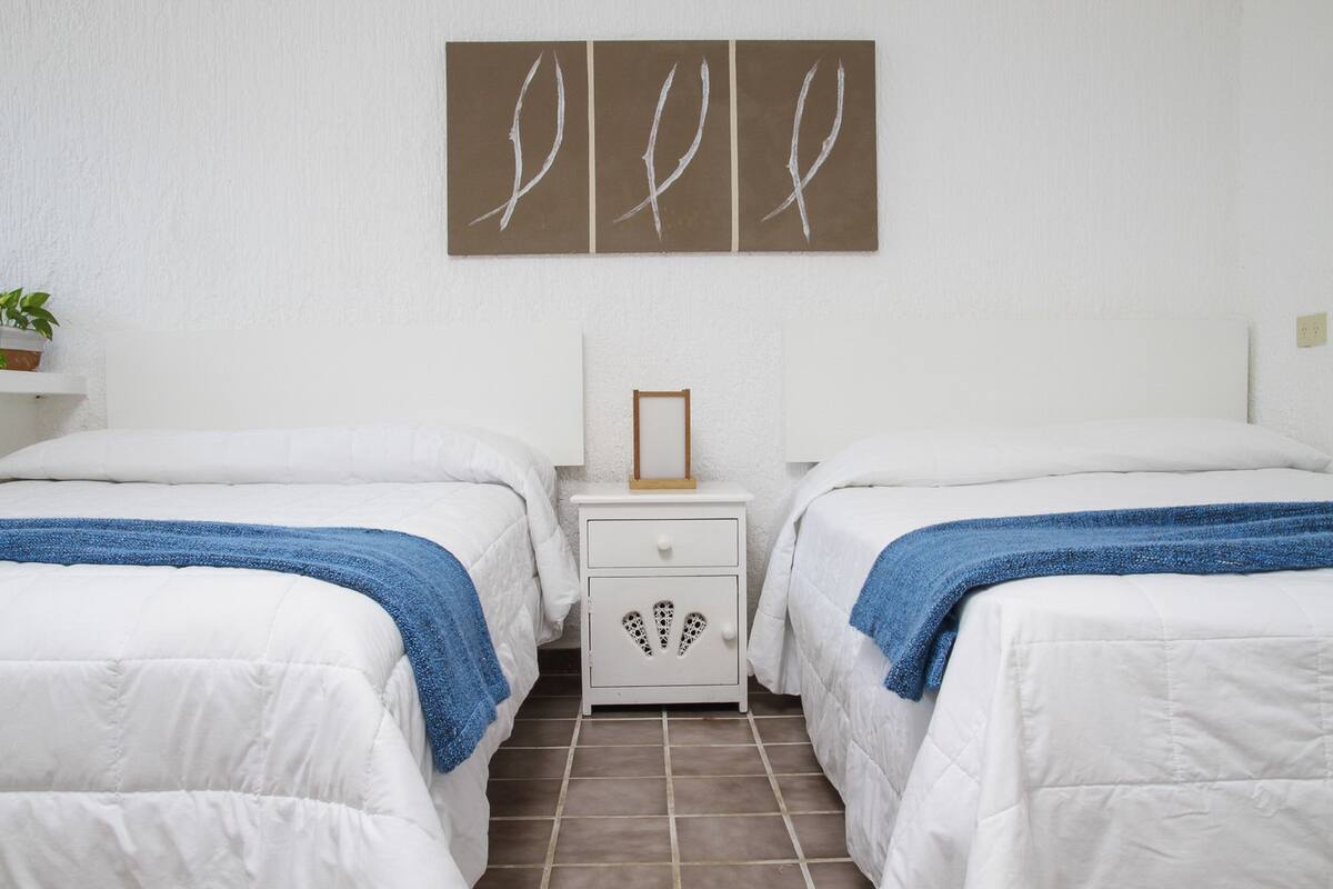 A hotel room with two beds, a nightstand, and a wall-mounted picture.