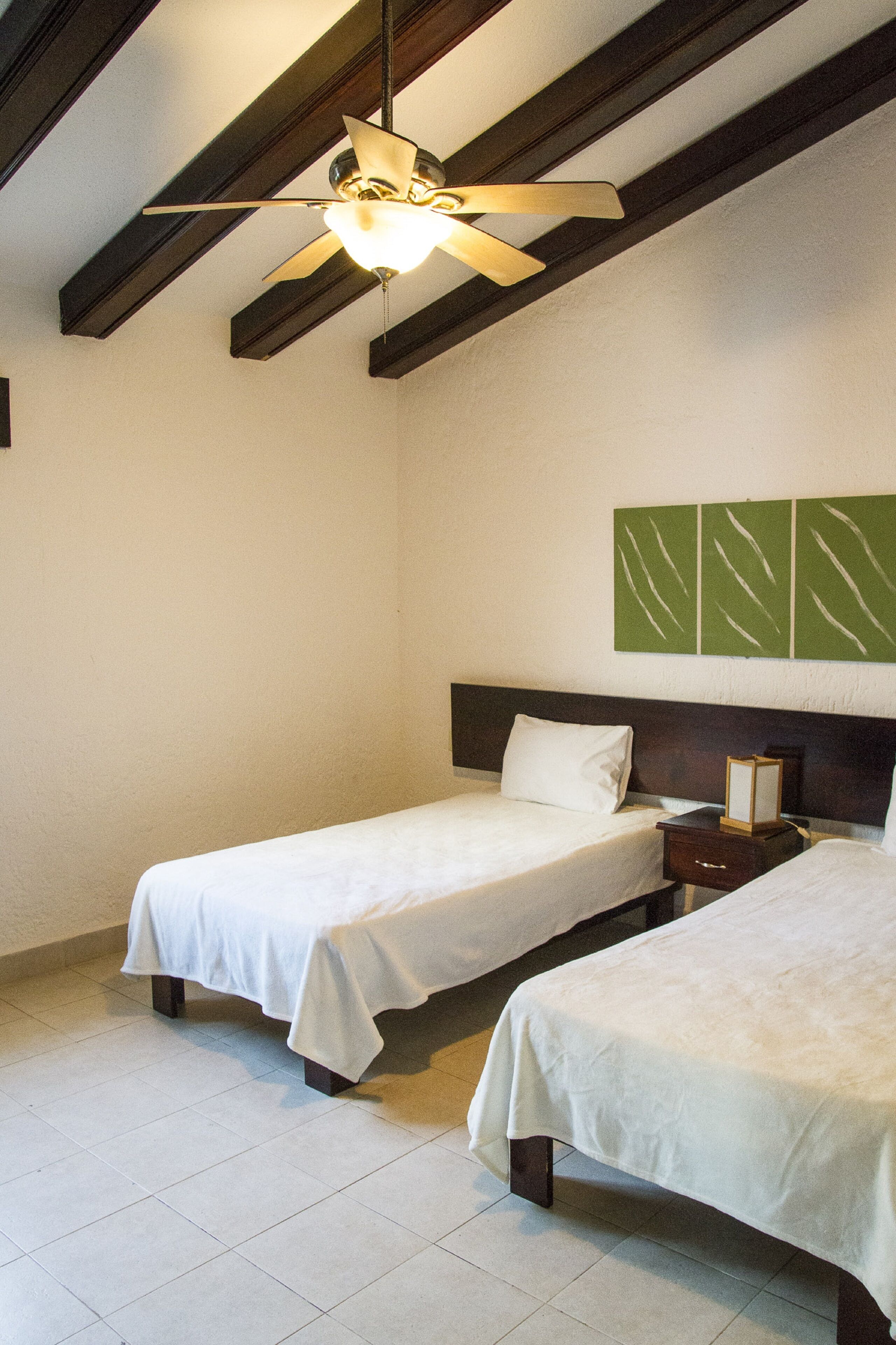 A hotel room with two single beds, a ceiling fan, and a wall-mounted artwork.