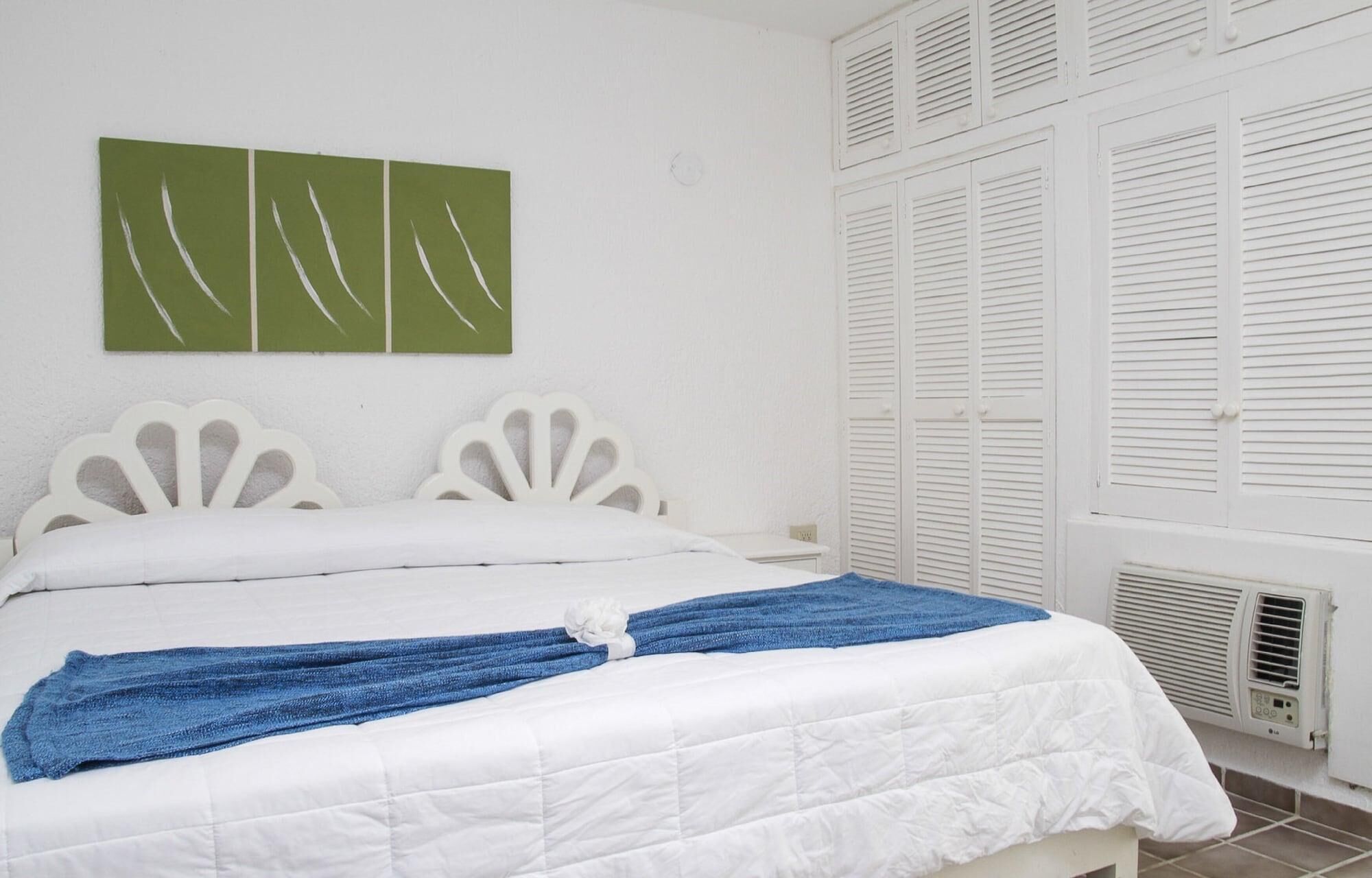 A bed with white headboard and footboard, a blue towel, and a green abstract painting on the wall.