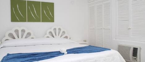 A bed with white headboard and footboard, a blue towel, and a green abstract painting on the wall.