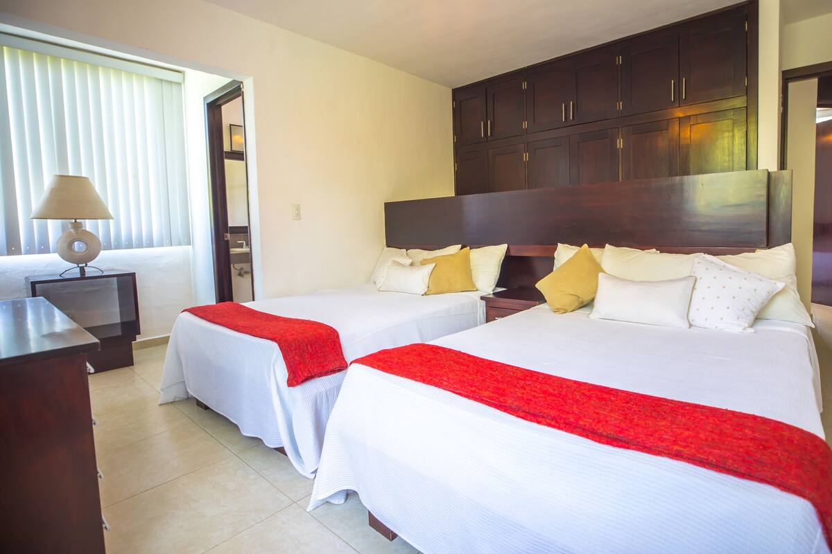 A hotel room with two beds, a desk, and a large wardrobe.