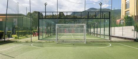 A fenced soccer field with a goalpost, surrounded by a netted enclosure and a mountain backdrop.