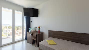 Ein Hotelzimmer mit Bett, Schreibtisch, Stuhl, einem an der Wand montierten Flachbildfernseher und einem großen Fenster mit Blick auf Gebäude und einen Berg.