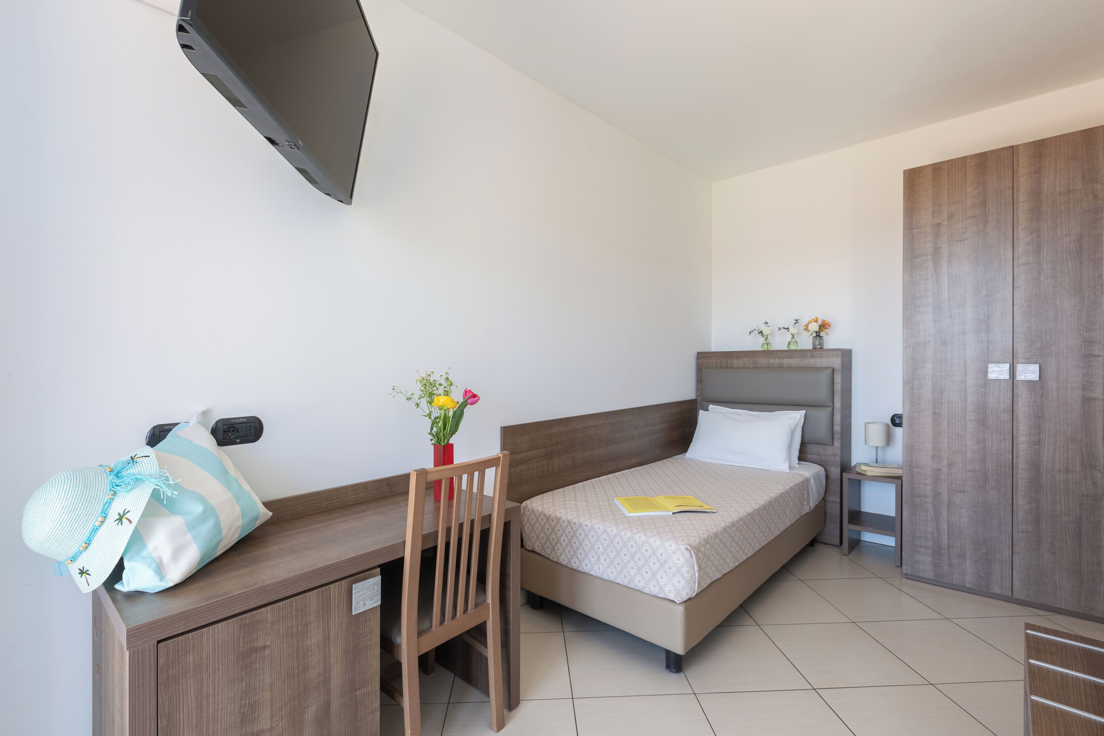 Een hotelkamer met een bed, een bureau, een stoel, een aan de muur bevestigde televisie en een kledingkast.