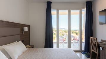 Una camera d'albergo con un letto, una scrivania, una sedia e un balcone con vista.