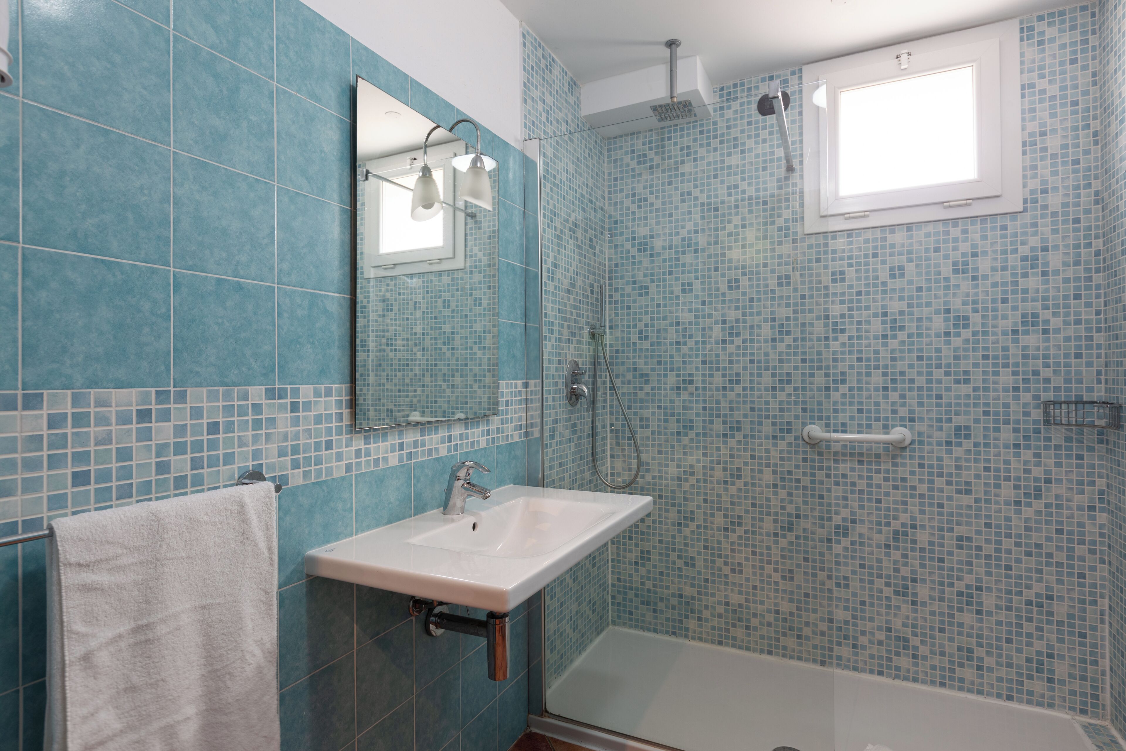Un bagno con un lavandino bianco, uno specchio e una doccia con finestra.