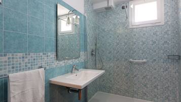 Un bagno con un lavandino bianco, uno specchio e una doccia con finestra.
