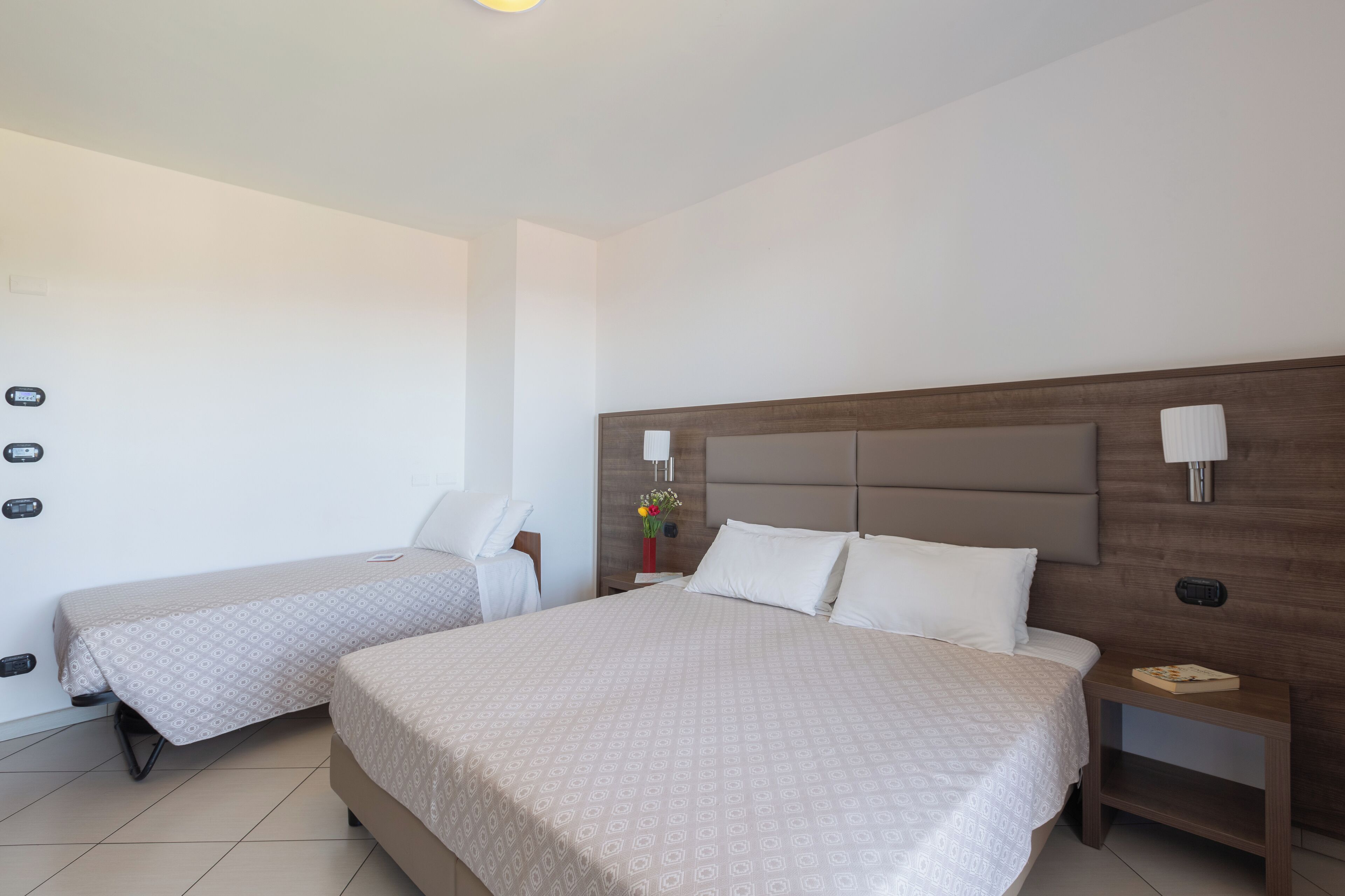 A hotel room with two single beds, a wooden headboard, bedside lamps, a nightstand, and a small table.