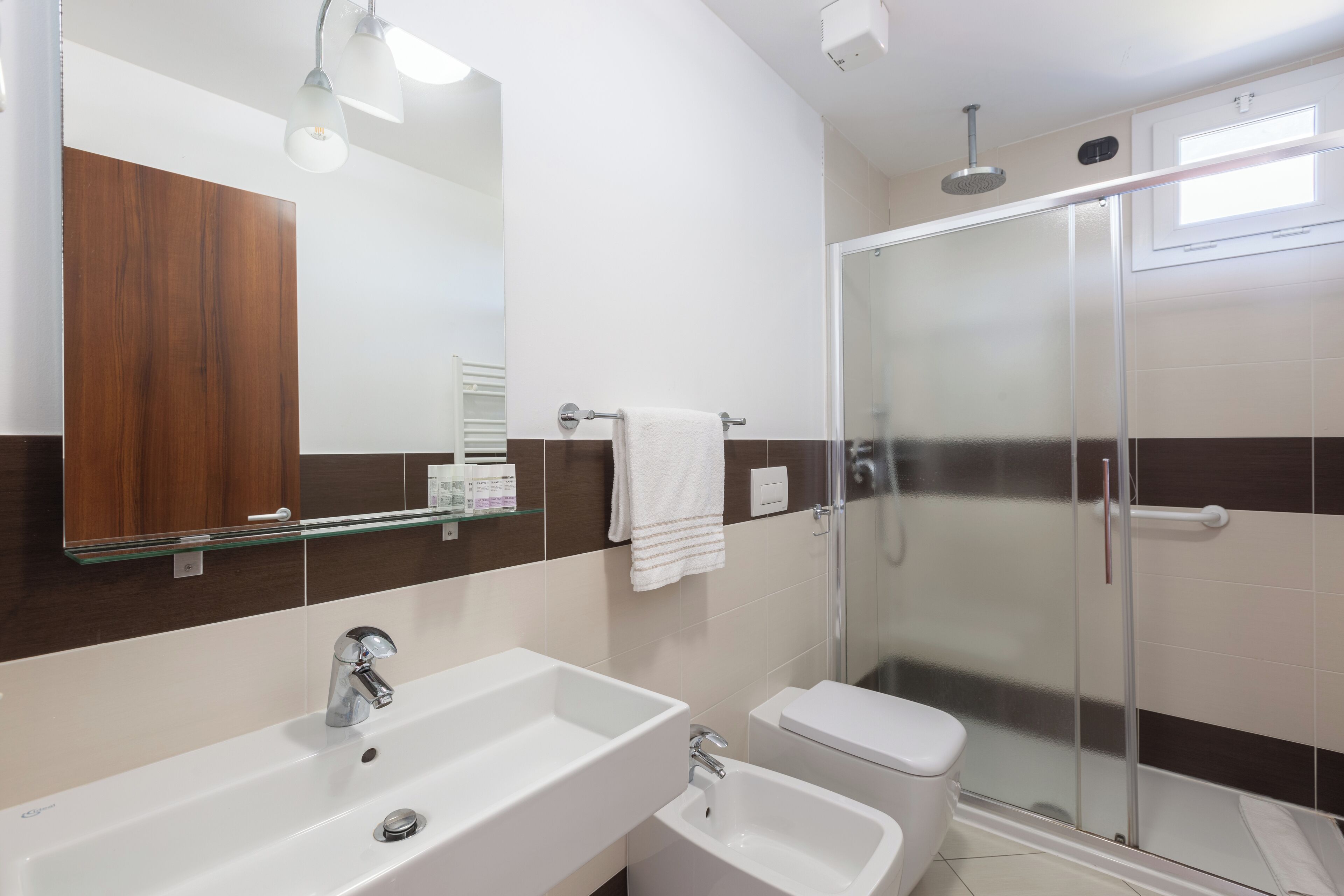 A modern bathroom with a large mirror, two sinks, a toilet, and a glass-enclosed shower.