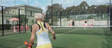 A tennis court with a net, a player in a yellow outfit, and a building in the background.
