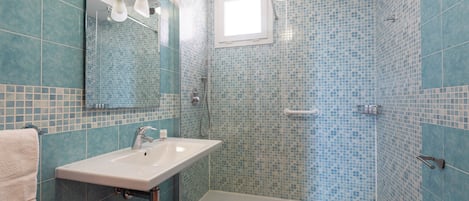 Une salle de bain avec un lavabo, un miroir, une douche et des murs carrelés.