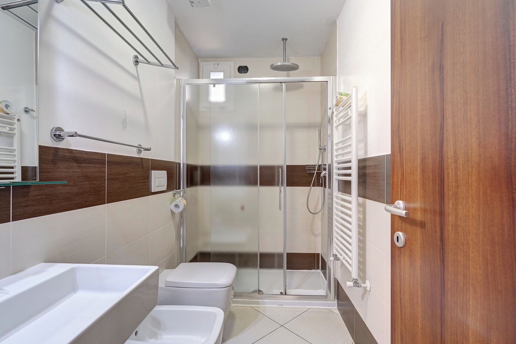 Un baño moderno con cabina de ducha de vidrio, tocador de madera y inodoro blanco.