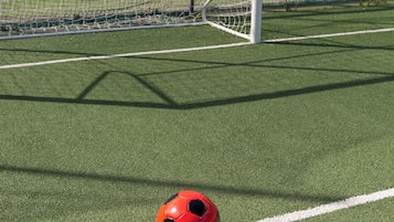 A soccer ball on artificial turf near a goalpost.