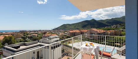 Un balcón con mesa y sillas, con vistas a una piscina y un paisaje montañoso.