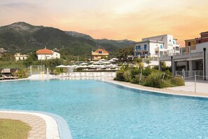 Une piscine entourée de bâtiments et de montagnes, avec des chaises longues et des parasols.