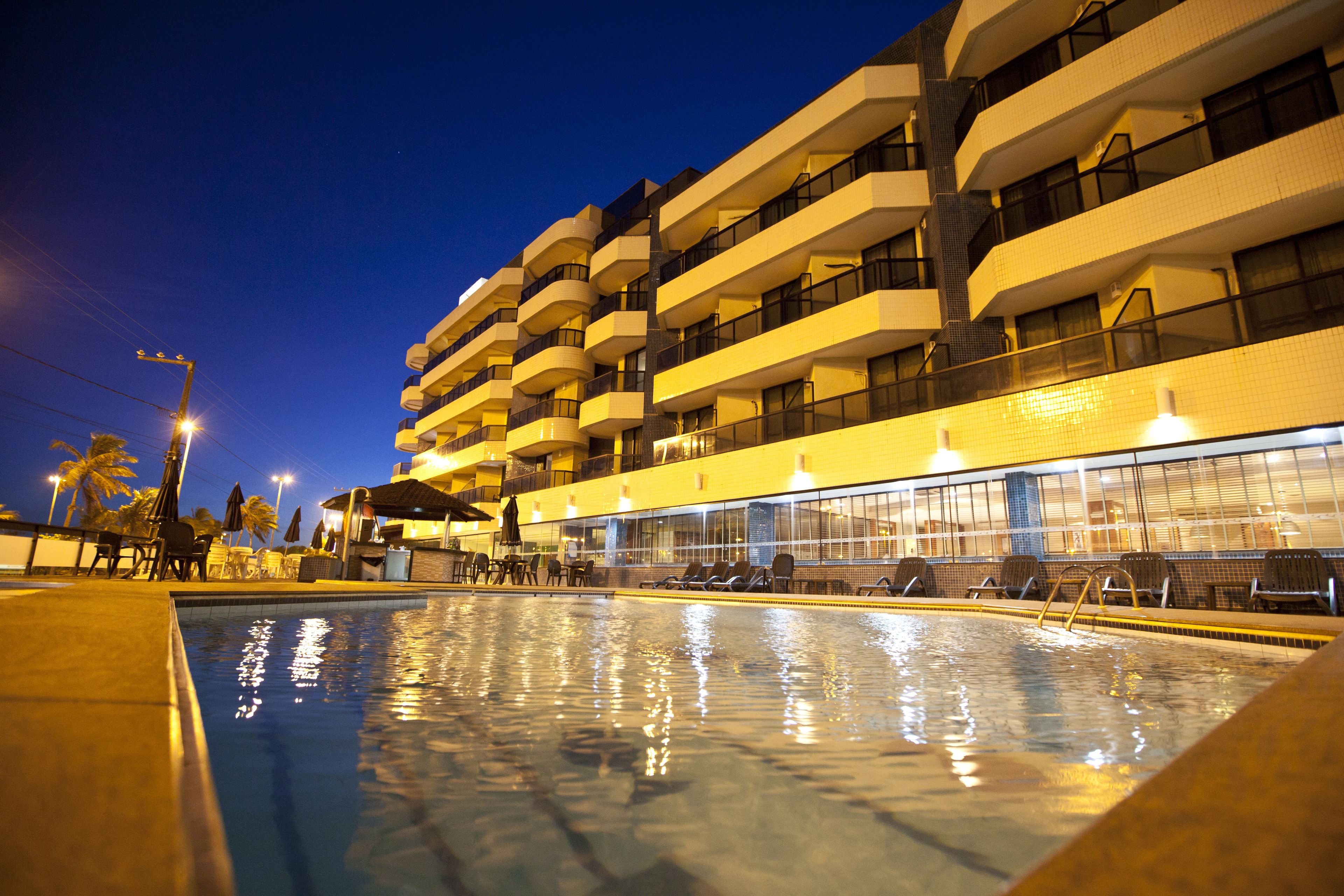 A hotel with a swimming pool, multiple balconies, and a well-lit exterior at night.
