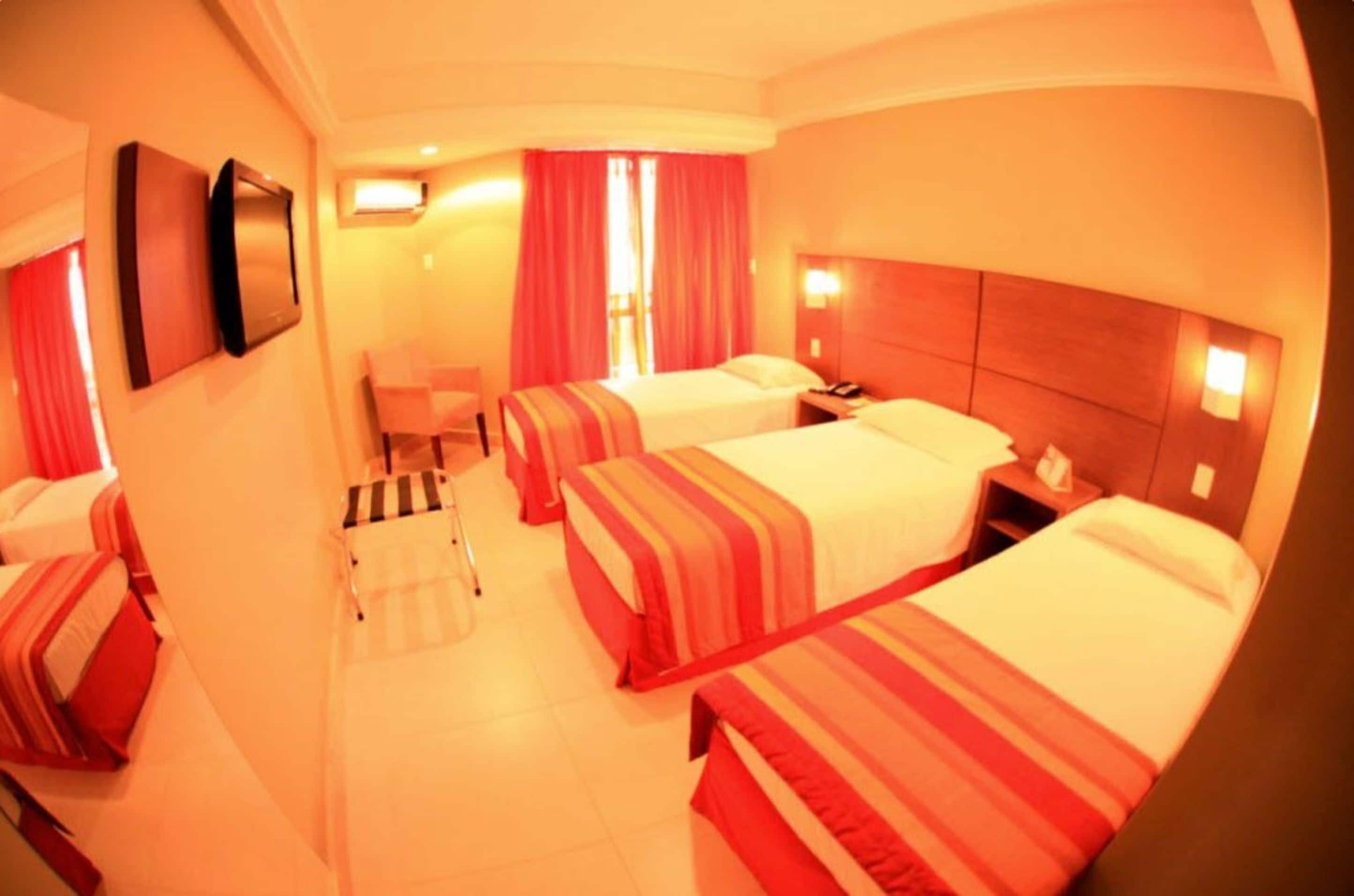 A hotel room with two beds, a desk, a chair, and a small table.