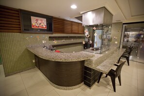 A modern kitchen with a curved granite countertop, wooden cabinets, and a stainless steel range hood. - Aquários Praia Hotel (Aracaju)