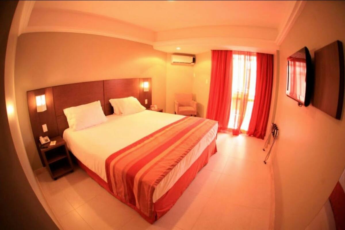A hotel room with a large bed, a nightstand, a chair, and a TV mounted on the wall.