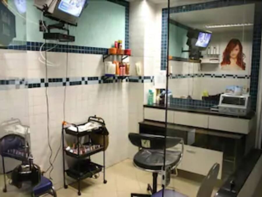 Un baño con lavamanos, espejo, repisas con artículos de aseo y un televisor.
