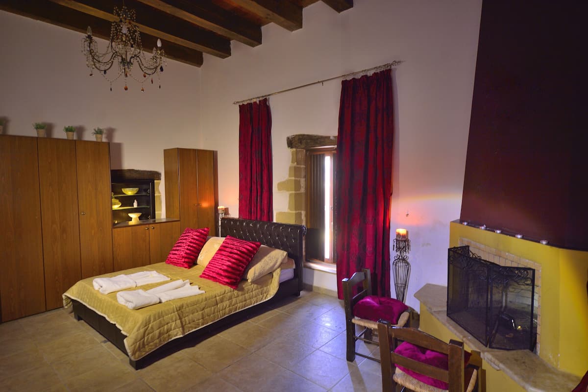 A bedroom with a bed, wooden wardrobe, red curtains, a fireplace, and a chandelier.