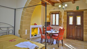 A room with a bed, a dining table with chairs, a fireplace, and a wooden ceiling. - Maria Villas (Kissamos)