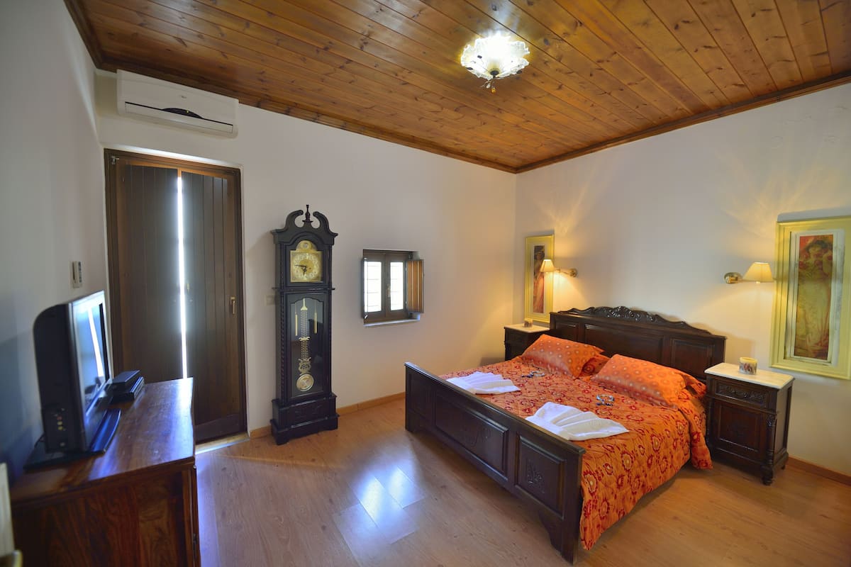 A bedroom with a wooden ceiling, a bed with an orange bedspread, a wooden dresser, a clock, and a television.