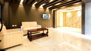 A lobby with a white sofa, a wooden coffee table, and a TV mounted on the wall. - LYNQ CICO (Kolkata)