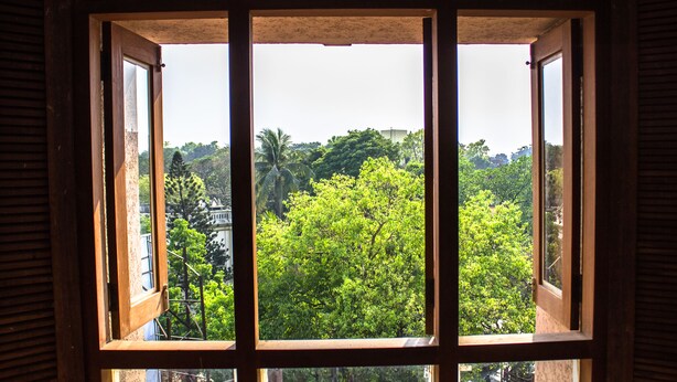 A window with a view of a lush green landscape and a building in the distance. - LYNQ CICO (Kolkata)