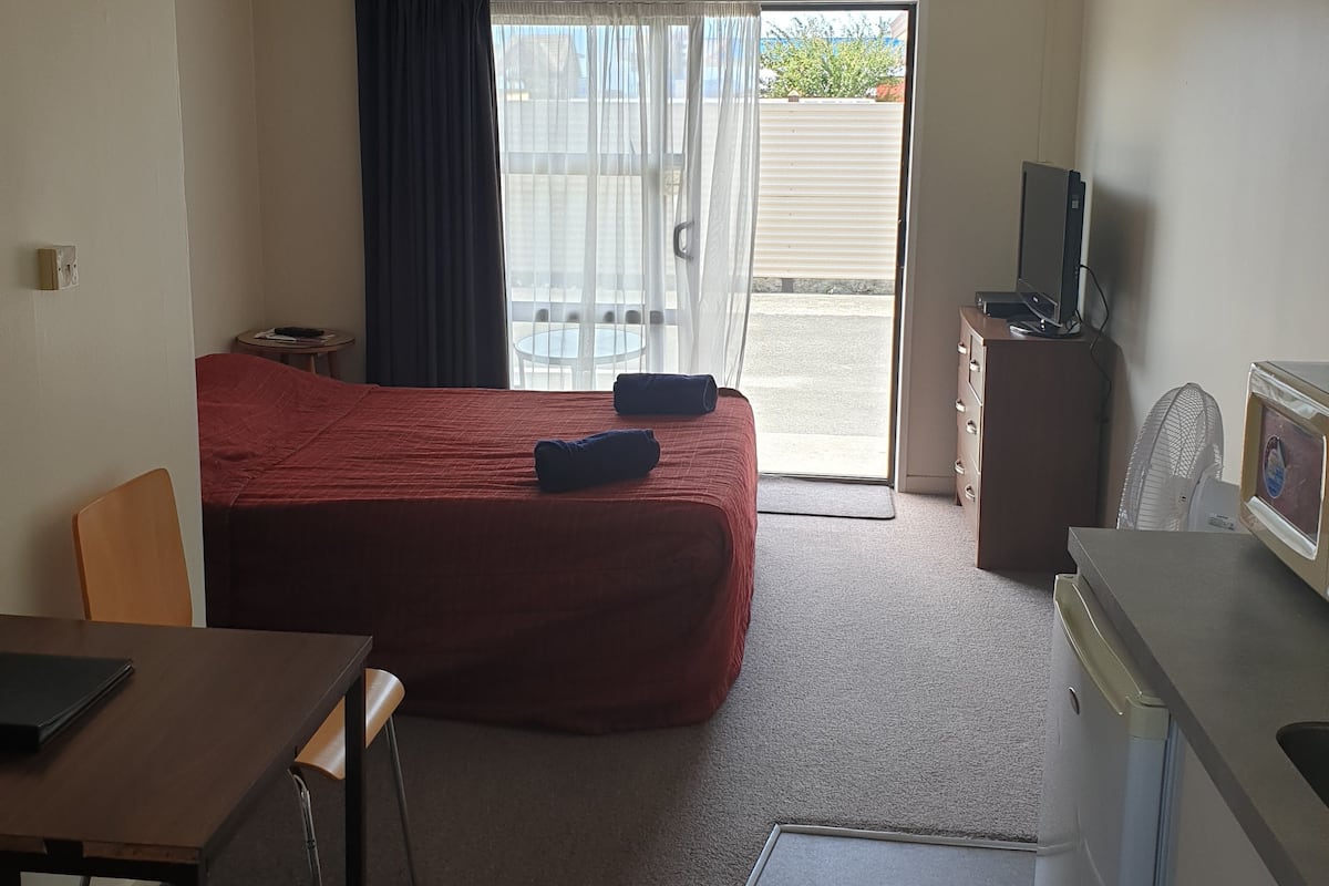 Ein Hotelzimmer mit Bett, Schreibtisch, Fernseher, Ventilator und einer Schiebetür zum Balkon.